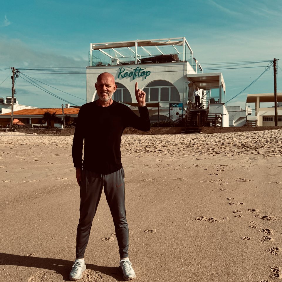 Floris wijst naar beachclub Rooftop op het strand